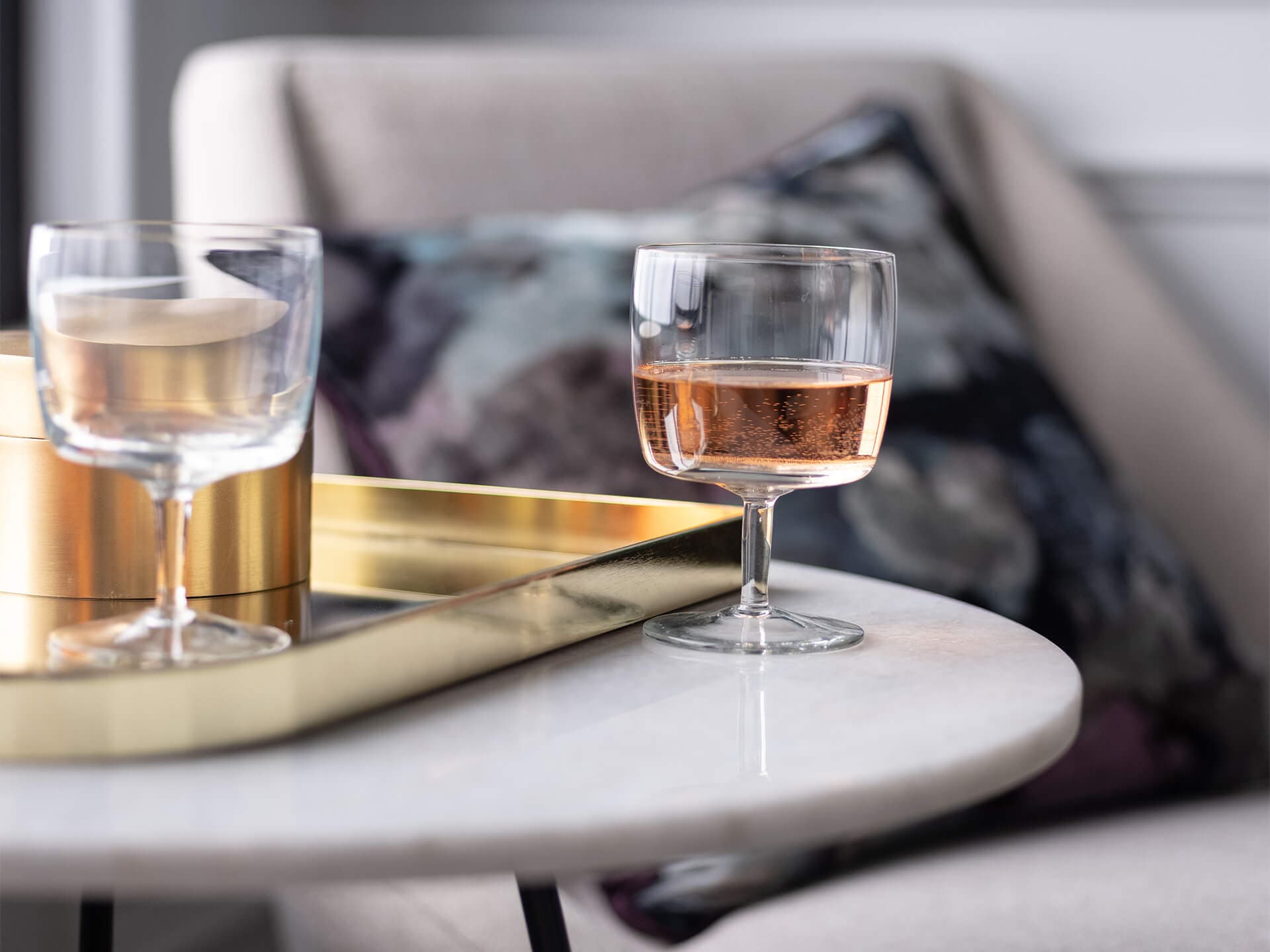 A glass of bubbling liquid on side table overlooking a chair set with a pillow