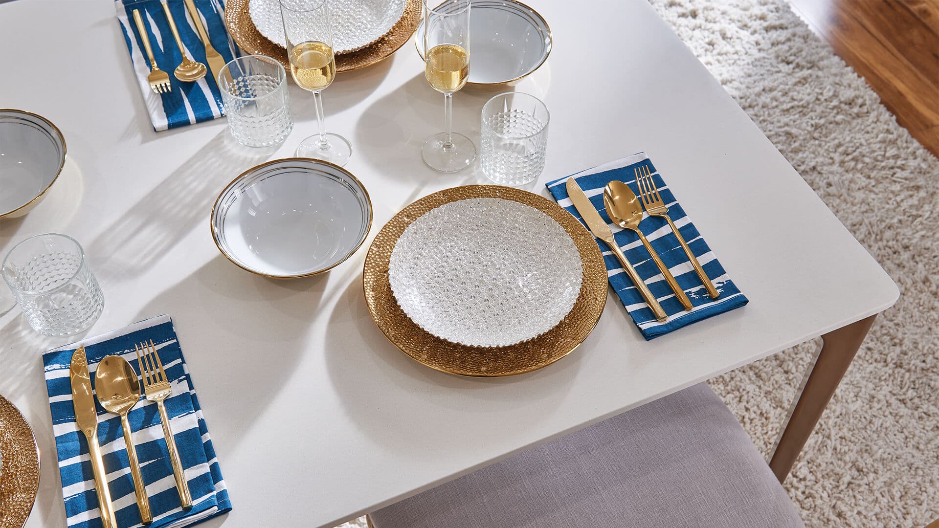 Table setting with white plates accented by gold flatware atop deep blue napkins and a bright wine